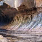 A natural rock formation resembling a canyon with flowing water at the bottom, surrounded by earthy colors and foliage.